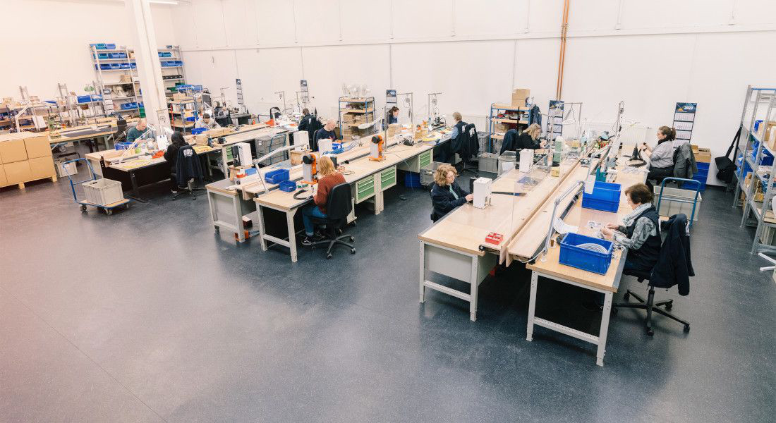 Produktionshal med flere arbejdsstationer, hvor medarbejderne bearbejder kabler.